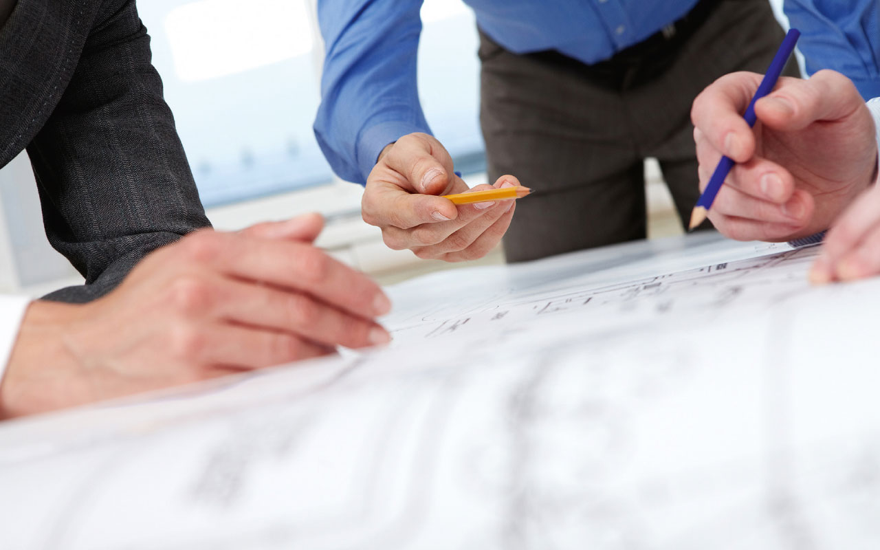 drei Personen an einem Schreibtisch mit Stiften in der Hand